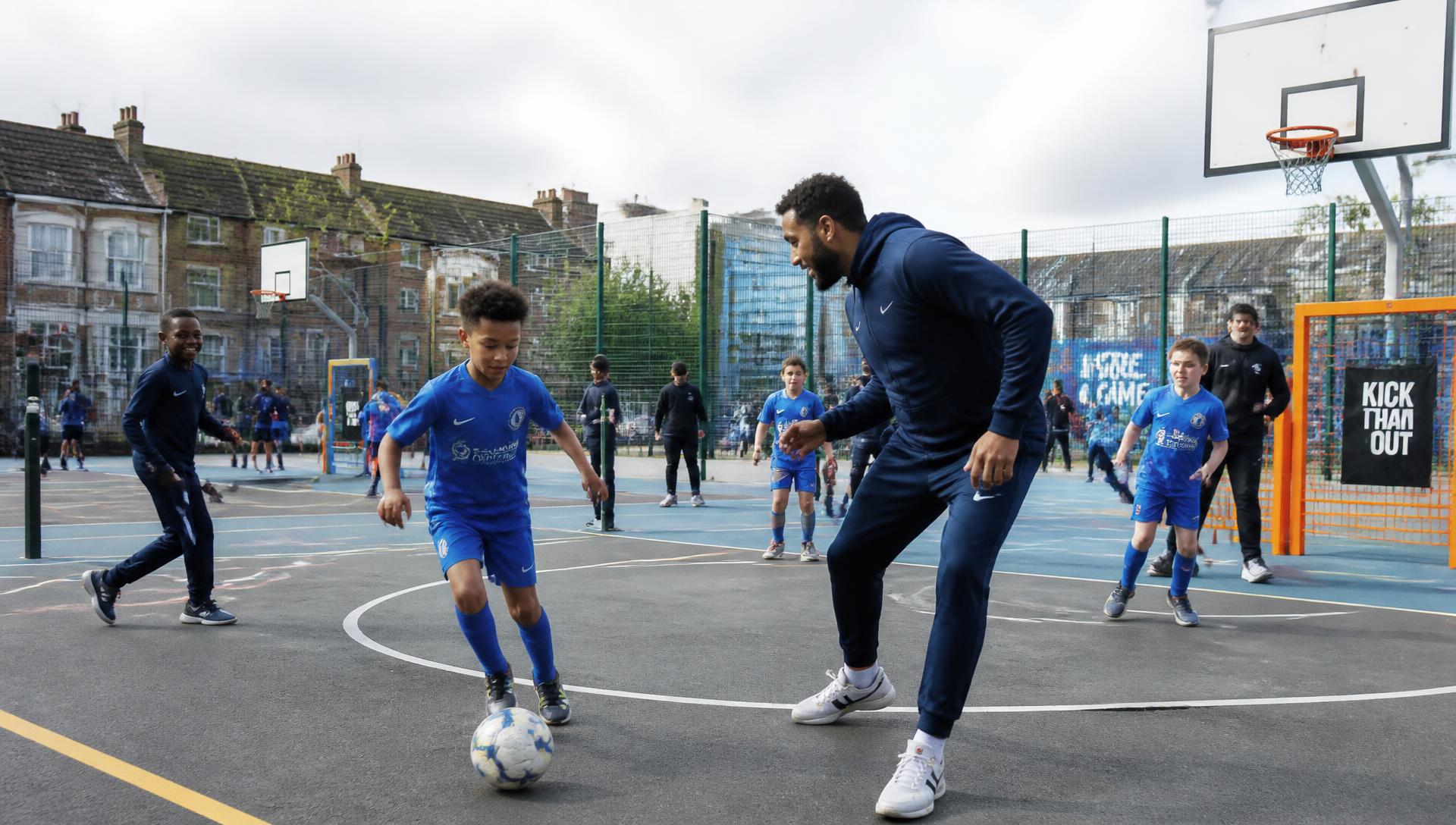 Young people and a coach playing football on a community court